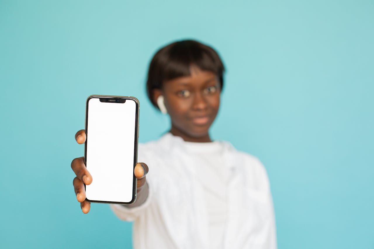 Portrait of a young woman holding a smartphone with a blank screen against a blue background.